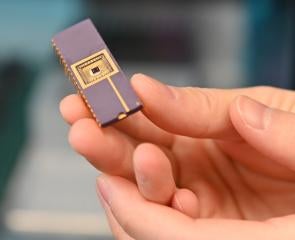 A hand holding a small chip that has gold circuits on the surface