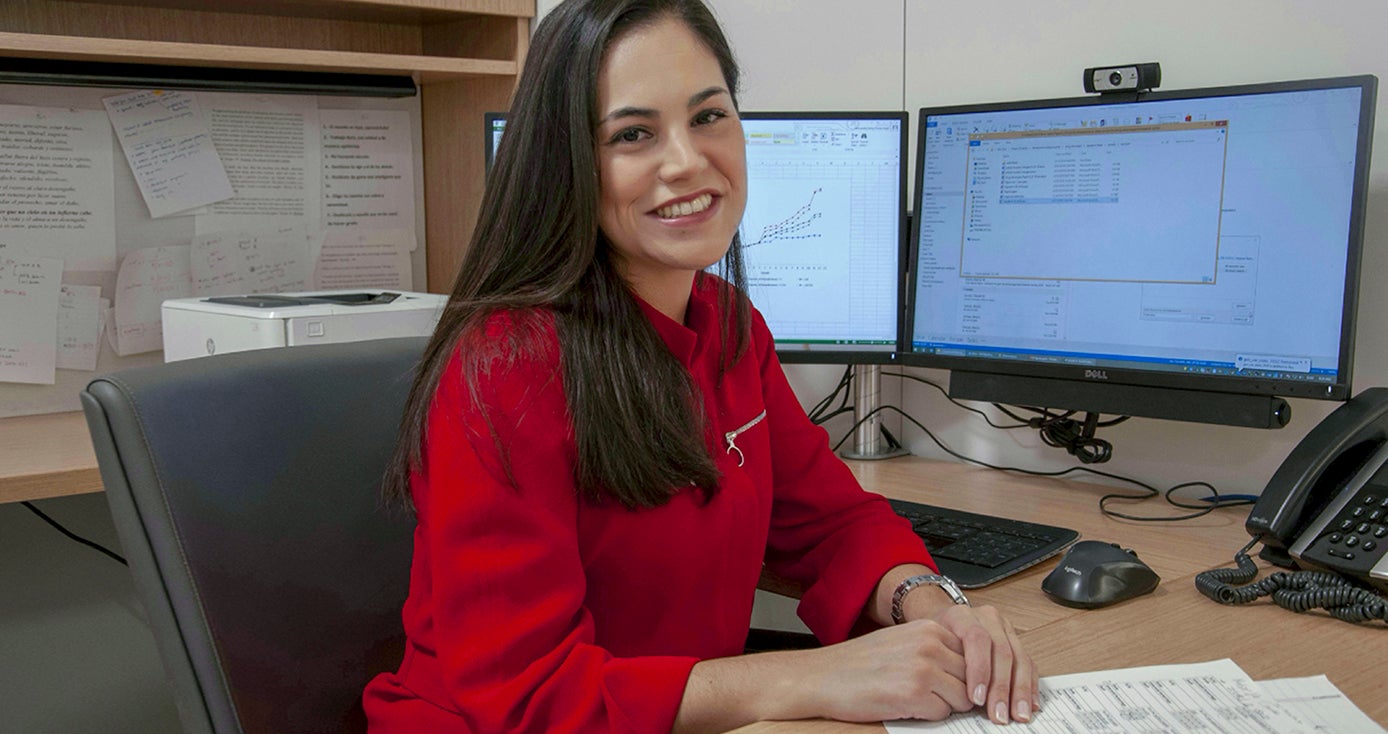 Hernandez in a red blouse in front of computer monitors