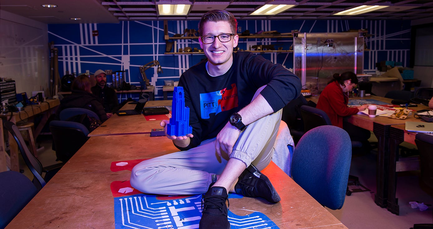 O'Brien sitting on a table in the Makerspace, holding a 3-D printed Cathedral of Learning