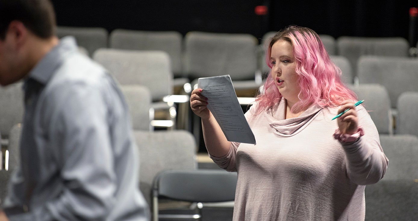 Chloe Torrence reading a script and holding a pen in a theater building setting