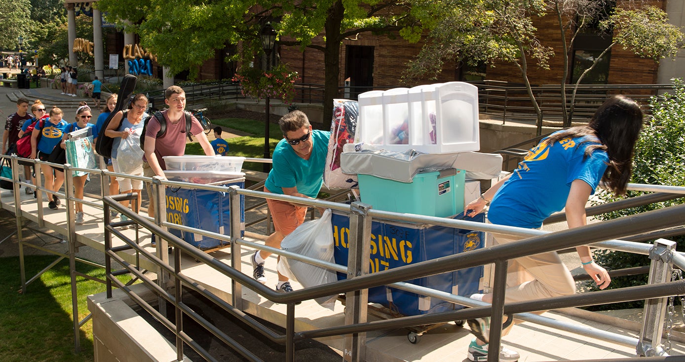 Several students pushing carts of belongings up a ramp
