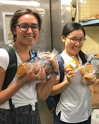 two women holding cookies in a campus kitchen