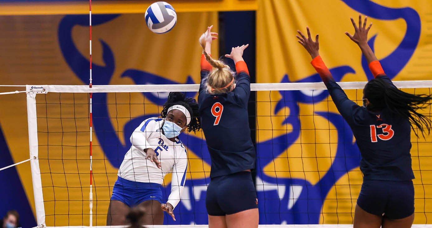 Four women play volleyball with a Pitt banner in the background