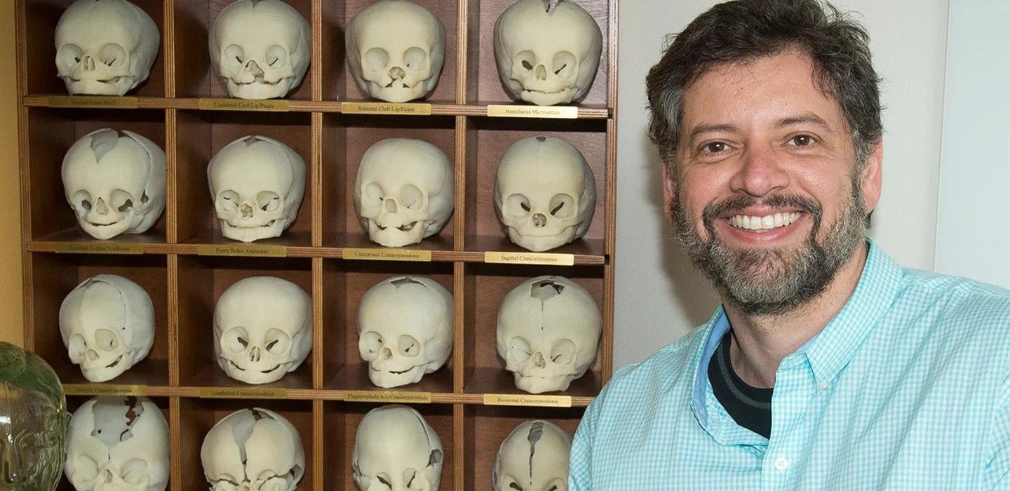 bearded man in front of a shelf of replica skulls