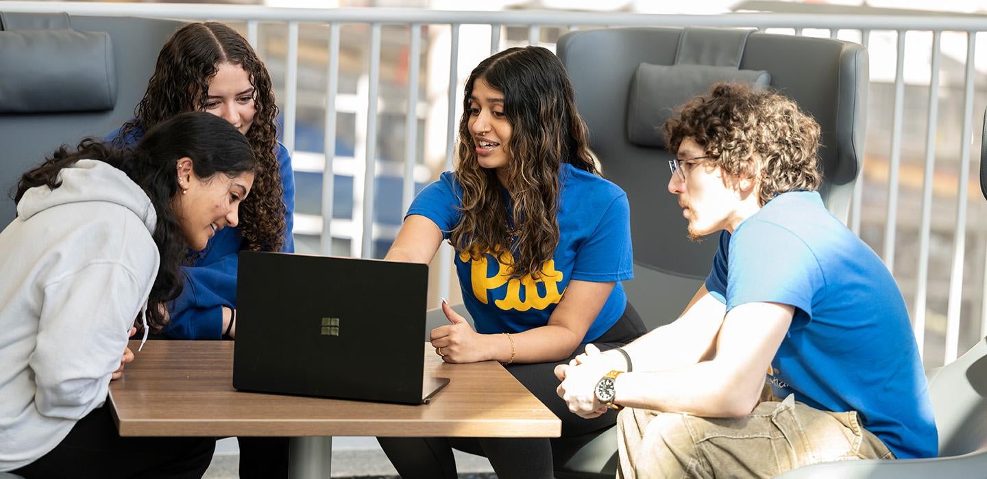 Four students huddle around a laptop