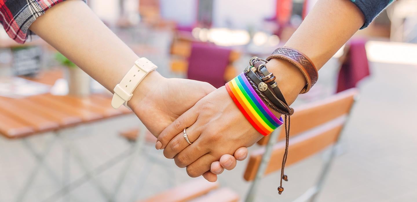 a close-up of two people holding hands, one wearing a watch and the other wearing a rainbow bracelet