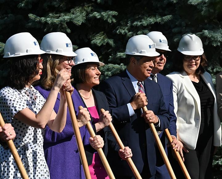 People in hard hats smile while holding shovels