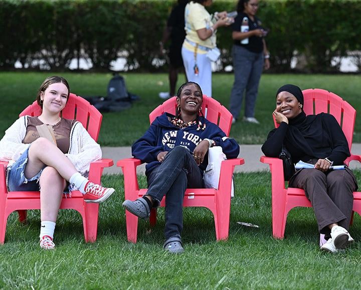 Three people sit smiling in red lawn chairs