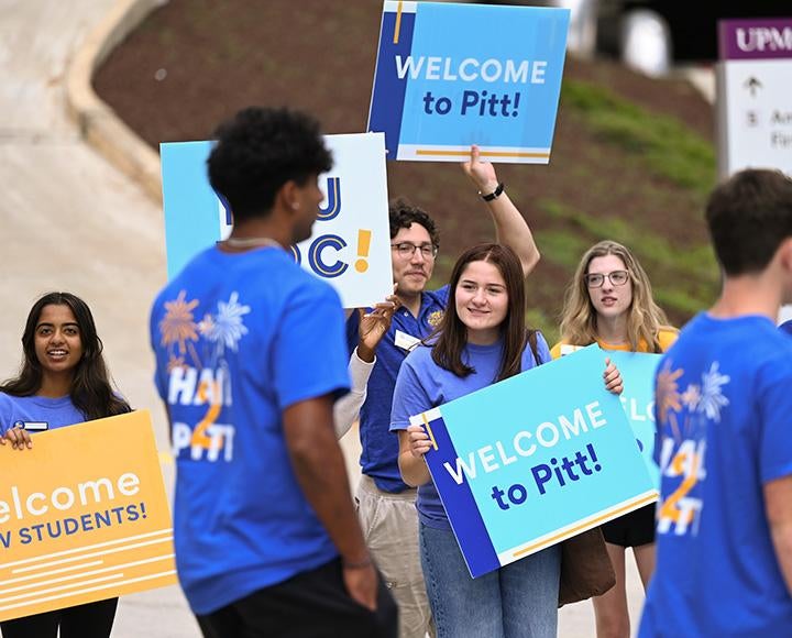 Students walk by people holding welcome signs