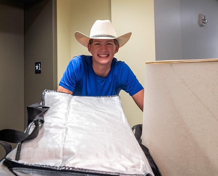 A student smiles with bags near an elevator