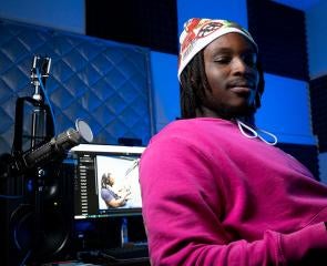 Kehinde sits in a podcast studio, surrounded by microphones and computer monitors