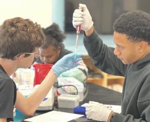 Two students pipette liquid into a vial 