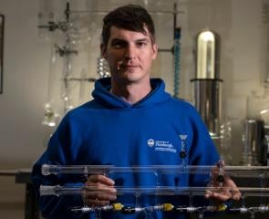 Ryan Tate poses with an apparatus of glass tubing