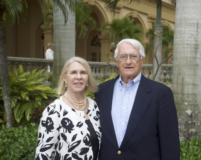 Woman and man in dressy attire pose in front of palm trees.