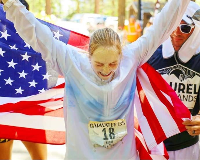 Frederick holds her arms up in front of an American flag after finishing Badwater