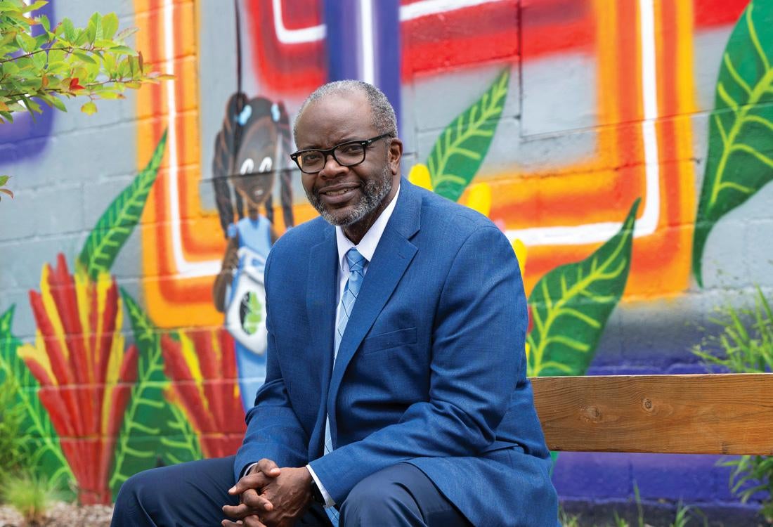 Man sitting on a bench in front of colorful mural.