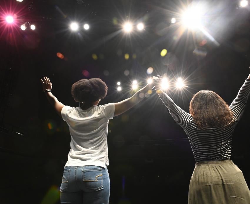 Two women holding hands in a spotlight
