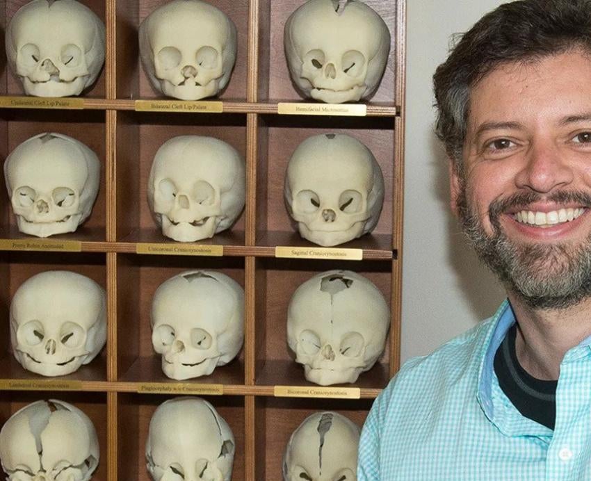 bearded man in front of a shelf of replica skulls