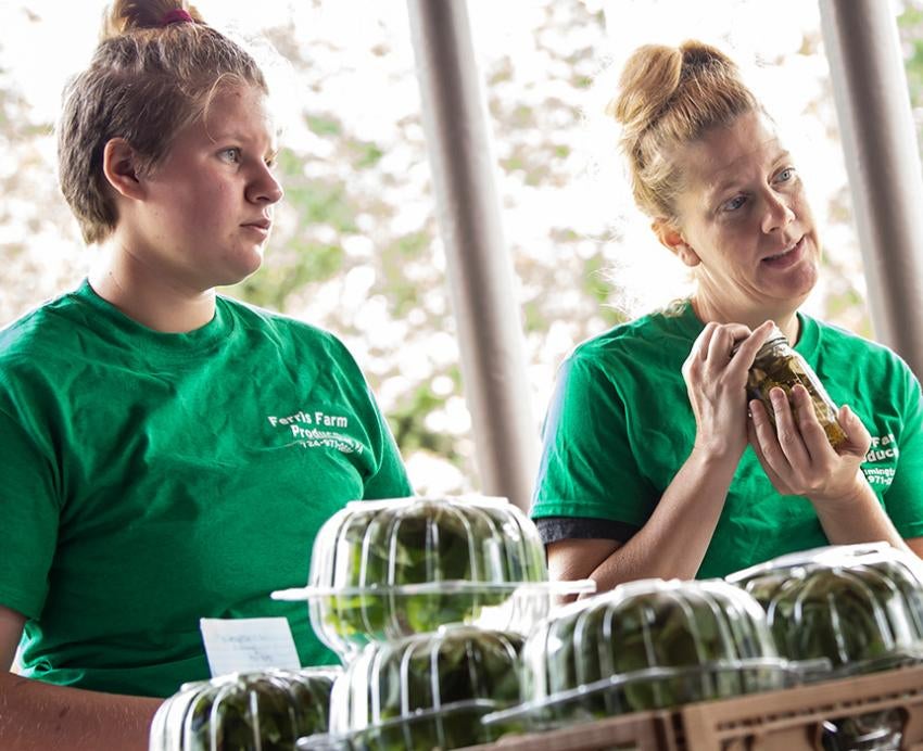 Two people in green shirts stand behind crates of greens in plastic containers