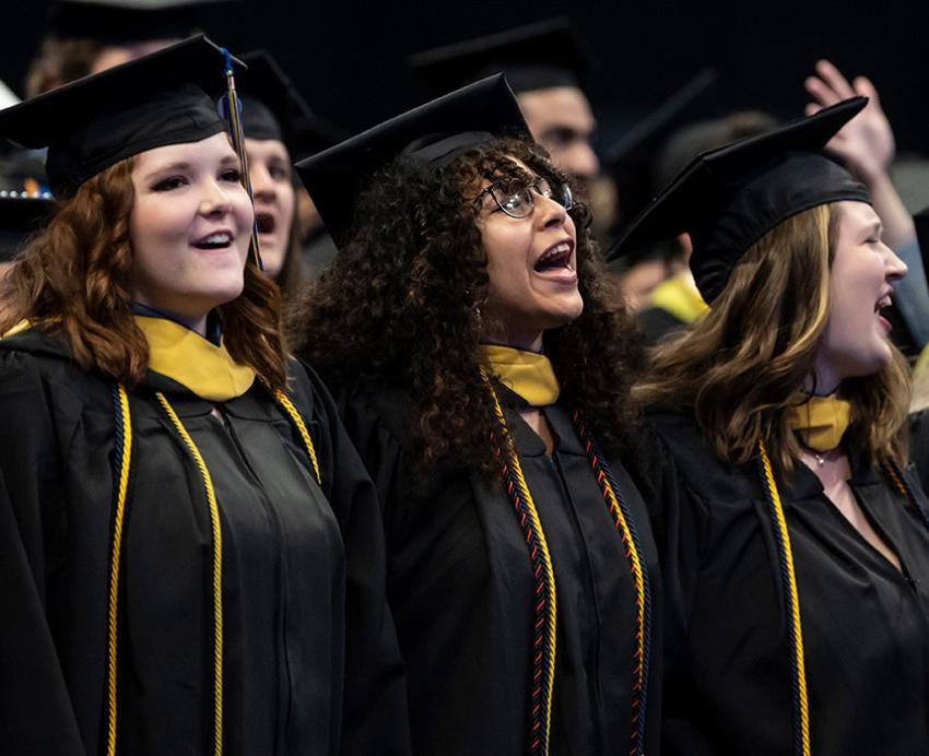 Graduates wearing regalia sing arm-in-arm