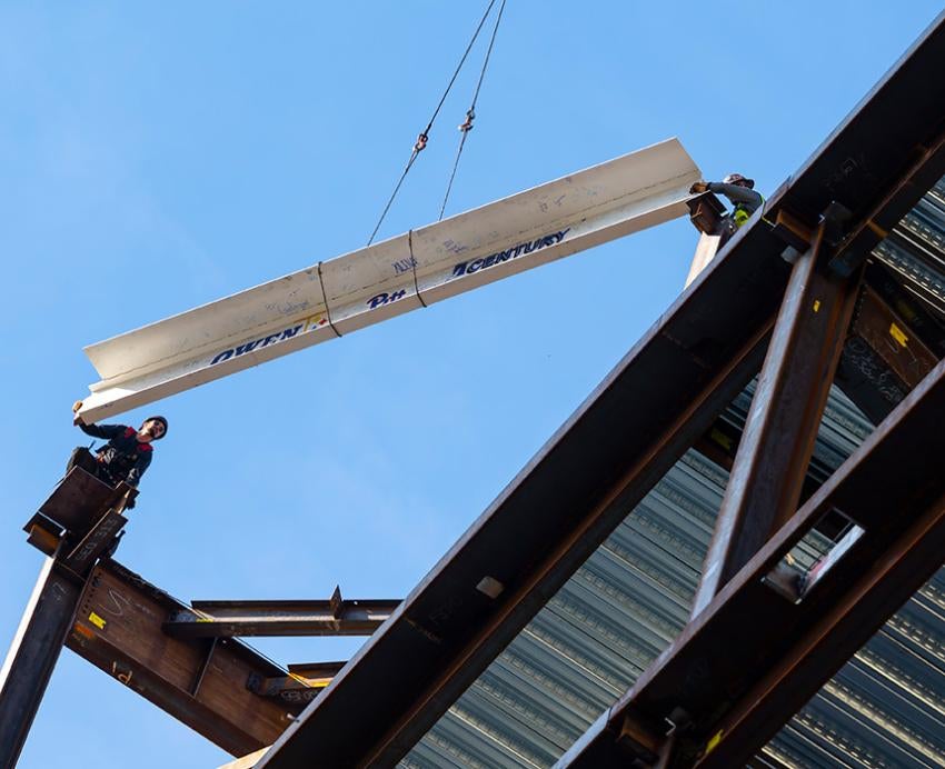 A beam is lifted to the top of a structure that is under construction