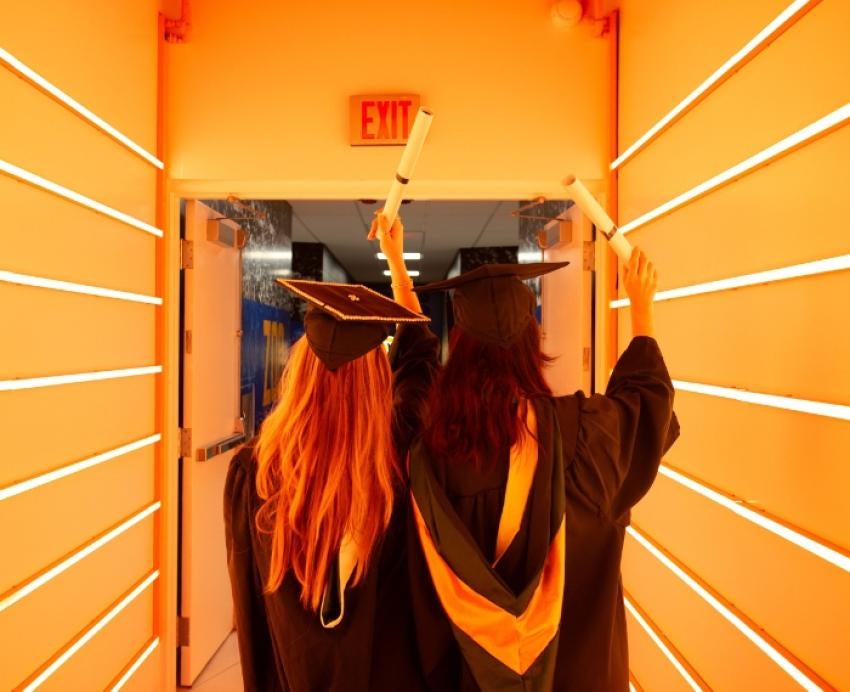 Two students face away from the camera, holding their degrees in the air.