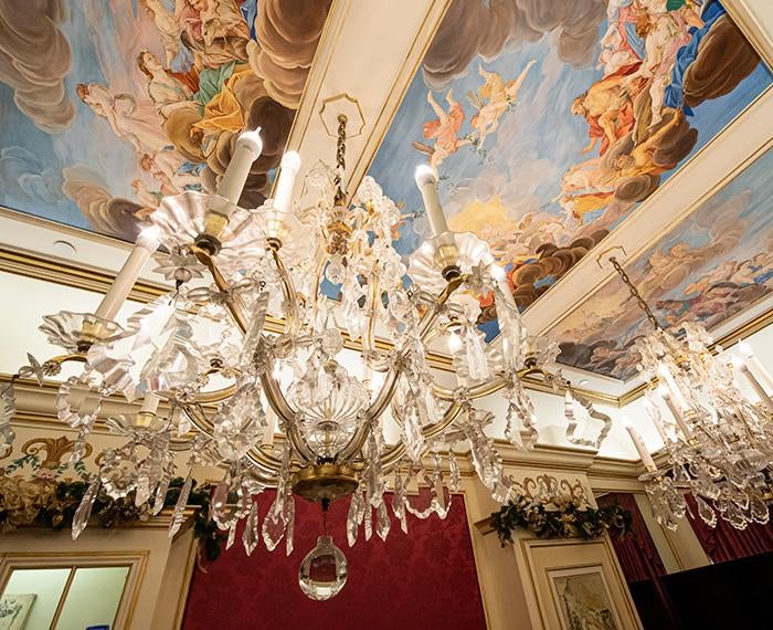 A chandelier hangs from a painted ceiling